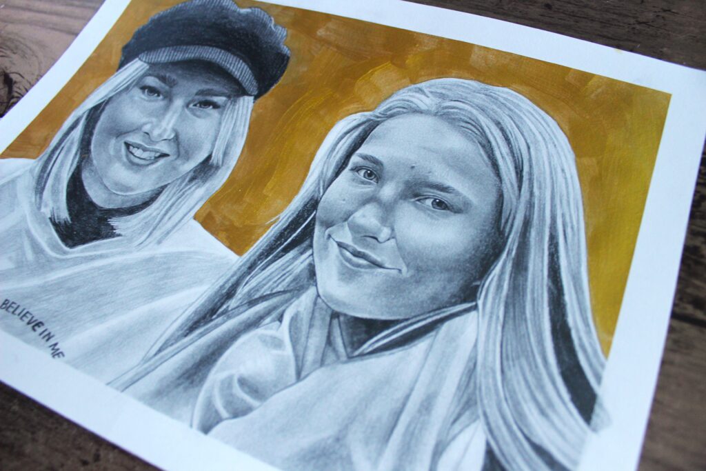 A detailed pencil drawing depicting two women with warm facial expressions. One woman, on the left, wears a black cap and a light-colored top, while the other, on the right, has long, straight hair and a light scarf. The background is a warm golden hue, and the words "BELIEVE IN ME" are faintly visible on the left side of the drawing.