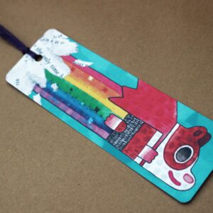 A vibrant bookmark featuring a colorful design, with a tassel, showcasing Super Poppy the guinea pig farting a rainbow.