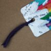 A vibrant bookmark featuring a colorful design, with a tassel, showcasing Super Poppy the guinea pig farting a rainbow.