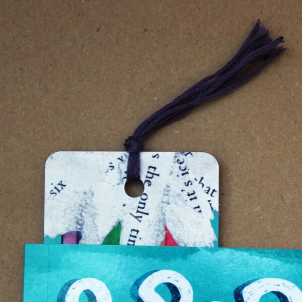 A book with a bookmark featuring a girl and a rainbow, along with a cute guinea pig named Super Poppy farting a rainbow. with a tassel.