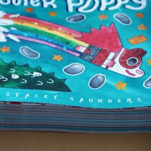 Stack of Super Poppy books topped with a rainbow and guinea pig, depicting a vibrant children's book by Stacey Saunders.